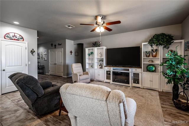 living room featuring a ceiling fan, visible vents, a fireplace, and wood finished floors