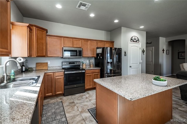 kitchen featuring appliances with stainless steel finishes, a kitchen island, a sink, and brown cabinetry