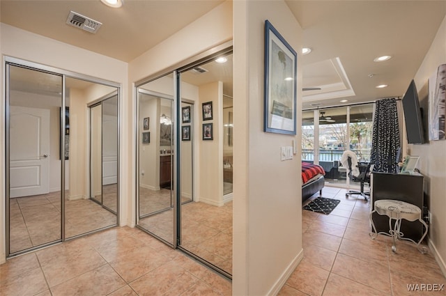 hall featuring a tray ceiling, light tile patterned flooring, recessed lighting, and visible vents