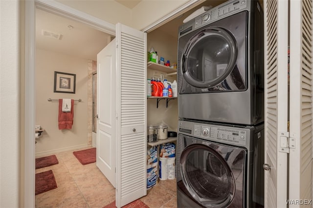 clothes washing area with visible vents, baseboards, laundry area, stacked washer and clothes dryer, and tile patterned floors