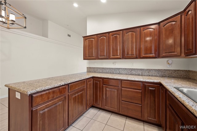 kitchen with light tile patterned floors, a peninsula, light stone counters, and decorative light fixtures