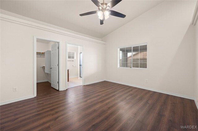 unfurnished bedroom featuring baseboards, lofted ceiling, dark wood-type flooring, a walk in closet, and a closet