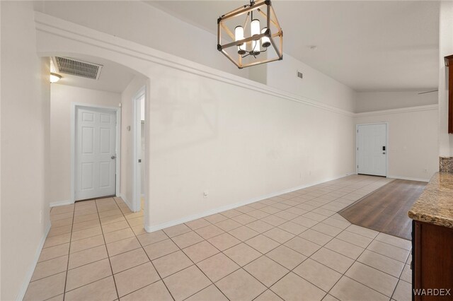 empty room with arched walkways, light tile patterned floors, lofted ceiling, and visible vents