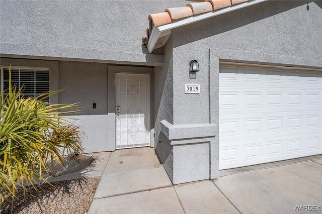 view of exterior entry with an attached garage and stucco siding