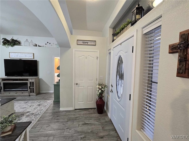 foyer featuring baseboards, dark wood-type flooring, and arched walkways