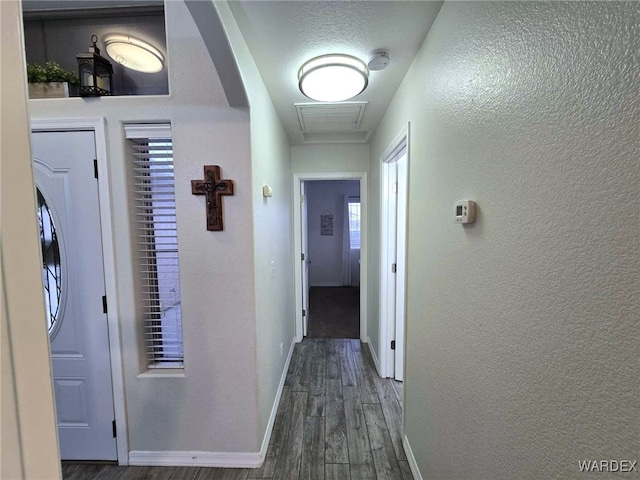 hall with visible vents, baseboards, a textured wall, and wood finished floors