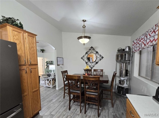 dining room with light wood-style floors, arched walkways, and baseboards