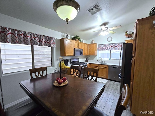 dining space with a ceiling fan, visible vents, vaulted ceiling, light wood-style floors, and a textured ceiling