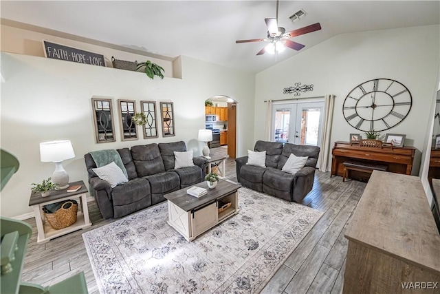 living area with arched walkways, ceiling fan, wood finished floors, french doors, and lofted ceiling