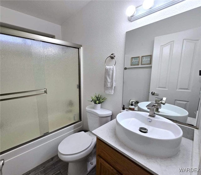 full bath featuring vanity, toilet, wood finished floors, and combined bath / shower with glass door