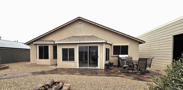 back of property featuring a patio, stucco siding, roof with shingles, and an outdoor fire pit