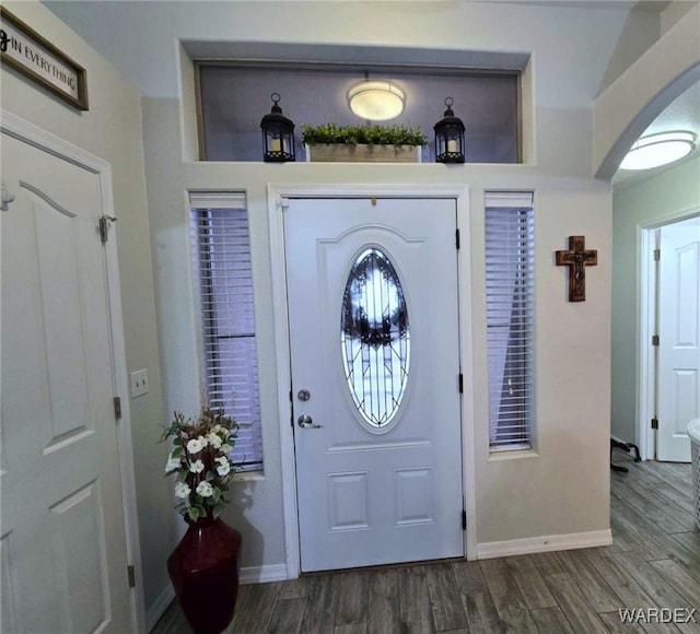 foyer featuring arched walkways, baseboards, and dark wood-style flooring