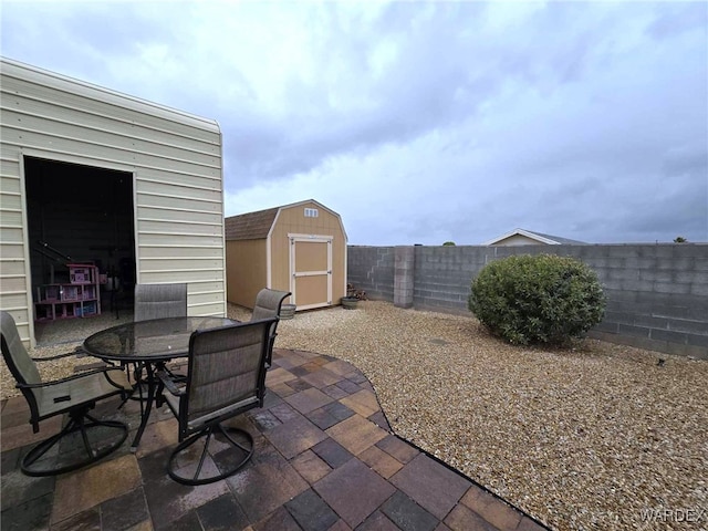 view of patio with a storage unit, a fenced backyard, outdoor dining area, and an outdoor structure