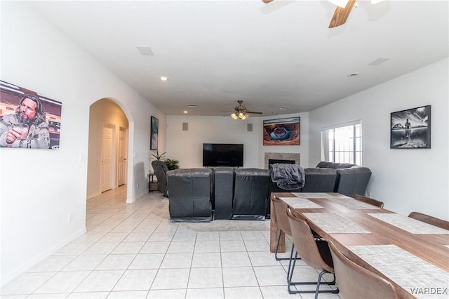 dining area with a ceiling fan, arched walkways, a fireplace, light tile patterned floors, and baseboards