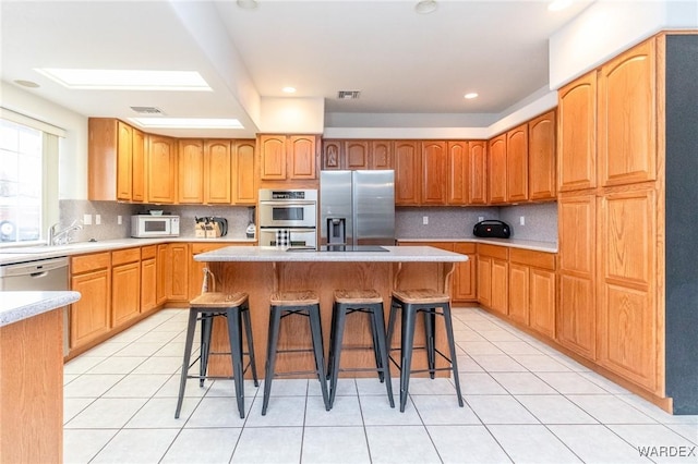 kitchen featuring light tile patterned floors, white microwave, light countertops, a kitchen bar, and stainless steel fridge