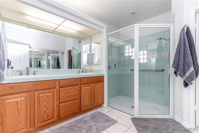 bathroom with tile patterned floors, double vanity, a stall shower, and a sink