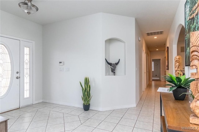 foyer with light tile patterned floors, arched walkways, visible vents, and baseboards