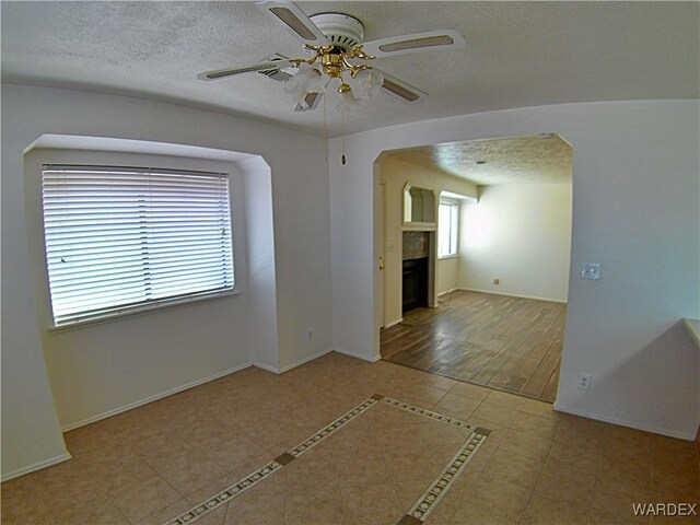 empty room featuring a textured ceiling, ceiling fan, light tile patterned floors, a fireplace, and baseboards