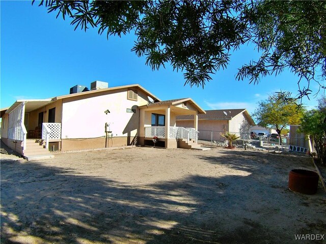 rear view of house with central AC unit, fence, and stucco siding