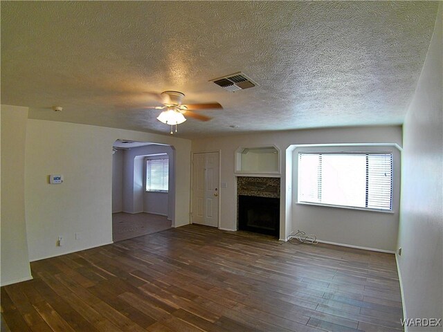 unfurnished living room featuring dark wood-style floors, a fireplace, visible vents, and arched walkways