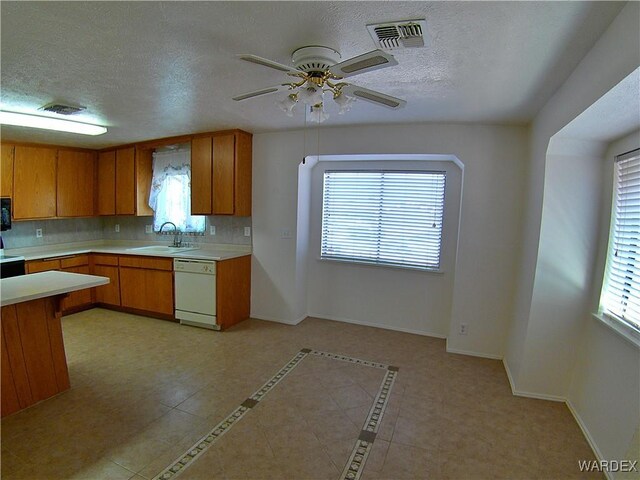 kitchen with visible vents, dishwasher, brown cabinets, light countertops, and a sink