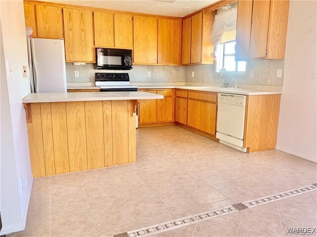 kitchen featuring black microwave, light countertops, freestanding refrigerator, dishwasher, and brown cabinetry