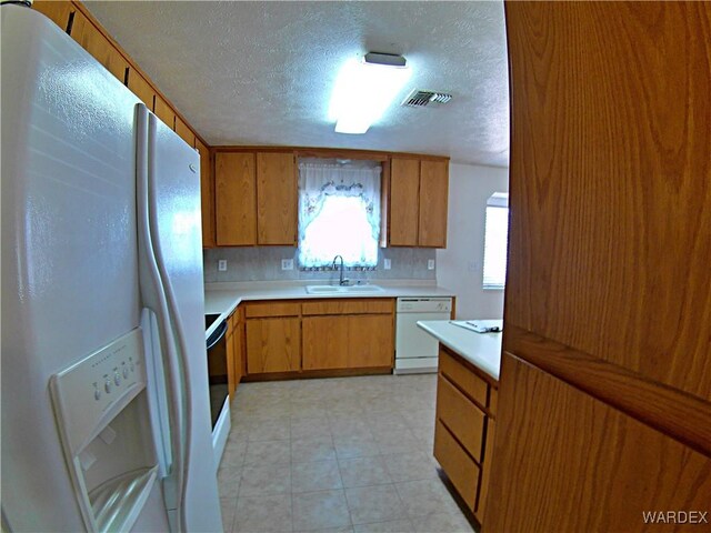 kitchen with brown cabinetry, white appliances, light countertops, and a sink