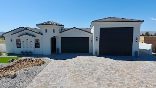 mediterranean / spanish home featuring an attached garage, fence, decorative driveway, and stucco siding