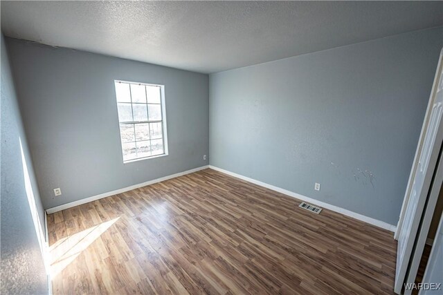 unfurnished room with baseboards, visible vents, dark wood finished floors, and a textured ceiling