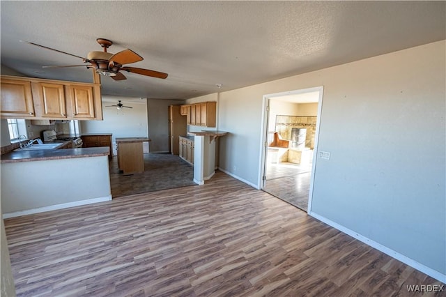 kitchen featuring a textured ceiling, a peninsula, a sink, baseboards, and light wood finished floors