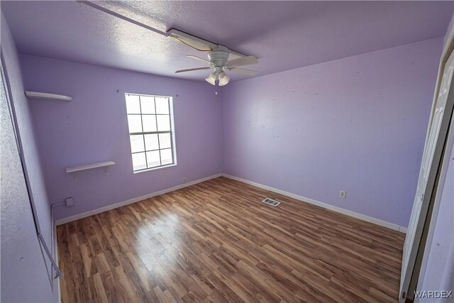 spare room featuring baseboards, visible vents, a ceiling fan, dark wood-type flooring, and a textured ceiling