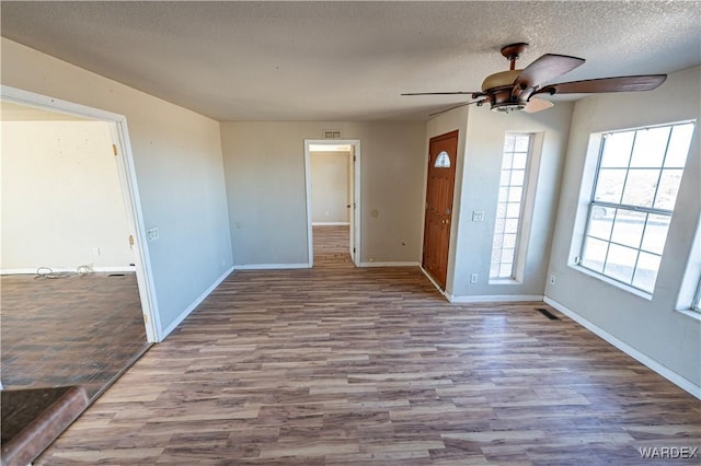 interior space with a ceiling fan, light wood-type flooring, a textured ceiling, and baseboards