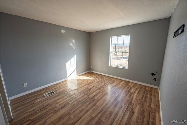 unfurnished room with dark wood-style floors, visible vents, and baseboards