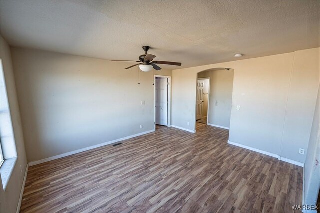 unfurnished room featuring baseboards, arched walkways, ceiling fan, wood finished floors, and a textured ceiling