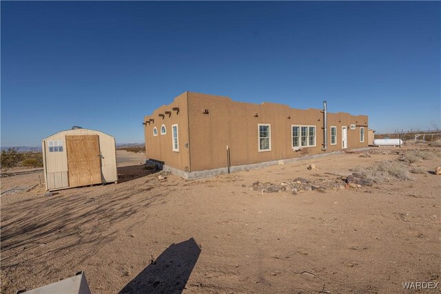 back of house featuring an outbuilding, stucco siding, and a storage unit