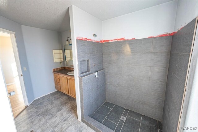 bathroom with tiled shower, a textured ceiling, and vanity