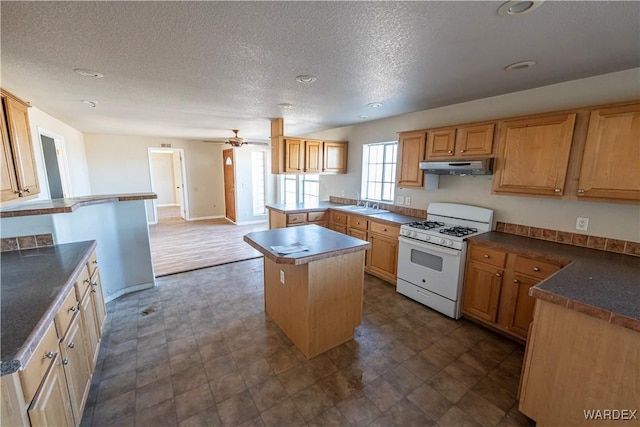 kitchen with a center island, dark countertops, a sink, white range with gas stovetop, and under cabinet range hood