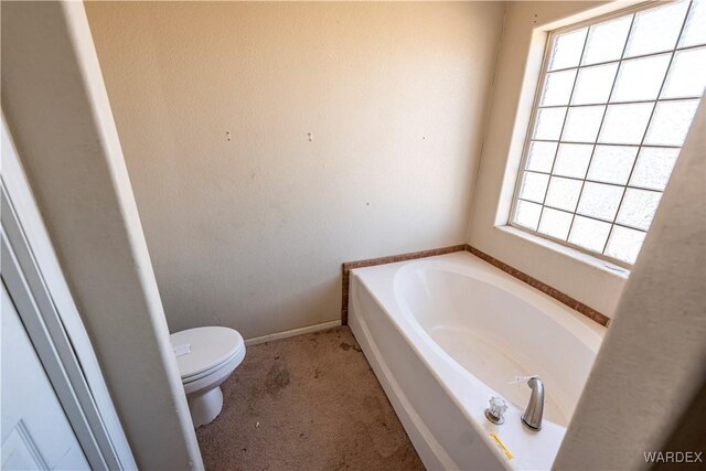 bathroom with a garden tub, toilet, and baseboards