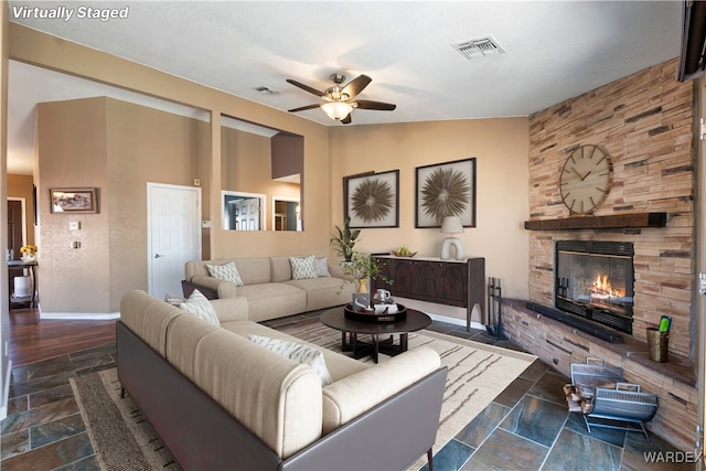 living area with a fireplace, visible vents, vaulted ceiling, and stone tile flooring