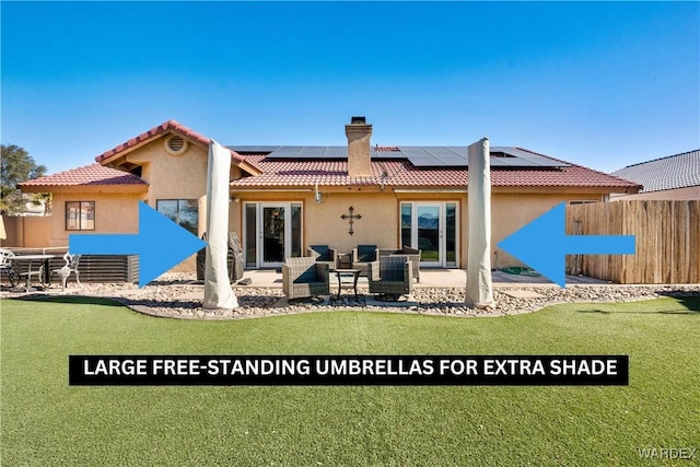 back of house featuring a chimney, stucco siding, roof mounted solar panels, a patio area, and fence