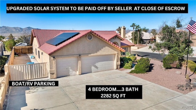 view of front of house with a mountain view, solar panels, fence, concrete driveway, and stucco siding