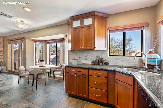 kitchen with a sink, visible vents, decorative backsplash, brown cabinets, and glass insert cabinets