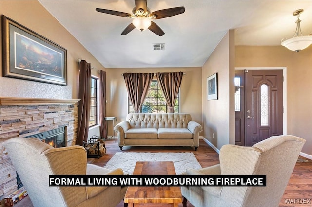 living room featuring baseboards, visible vents, wood finished floors, vaulted ceiling, and a fireplace