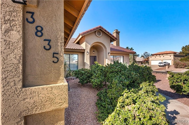 mediterranean / spanish-style house featuring a chimney, a tile roof, and stucco siding