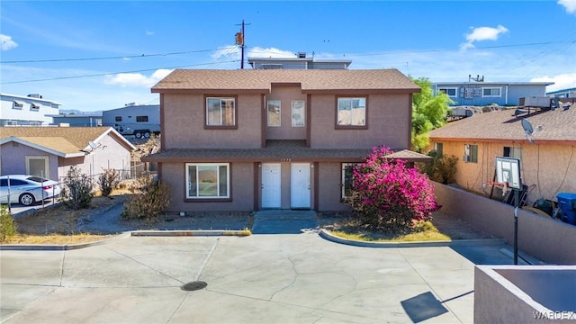 view of front of home with a shingled roof, fence, a residential view, stucco siding, and a patio area