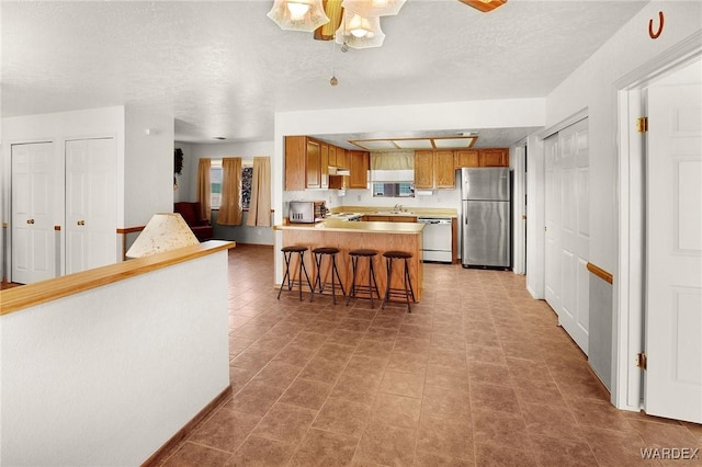 kitchen featuring stainless steel appliances, a breakfast bar, a peninsula, light countertops, and brown cabinets