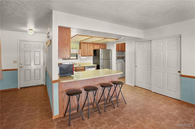 kitchen featuring washer / clothes dryer, a breakfast bar, freestanding refrigerator, a peninsula, and light countertops