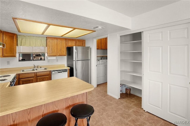 kitchen with dishwashing machine, freestanding refrigerator, a peninsula, light countertops, and a sink