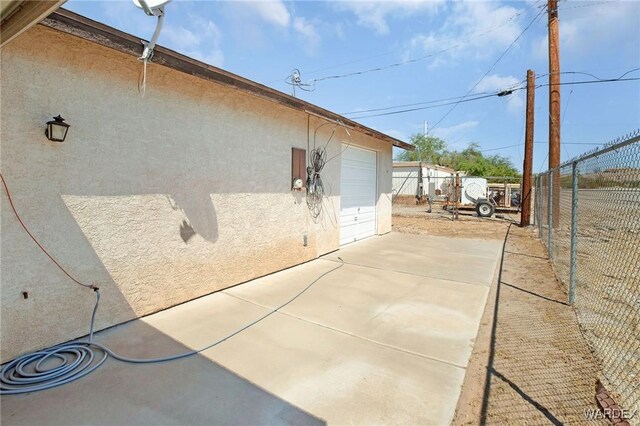 view of side of property featuring driveway, a garage, fence, and stucco siding