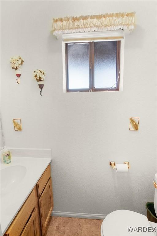 half bathroom with baseboards, vanity, and toilet